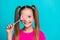 Portrait of toothy beaming nice small girl dressed pink t-shirt holding lollipop on eye smiling isolated on turquoise