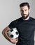 Portrait of tough confident soccer player wearing black jersey t-shirt holding ball under his arm