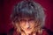 Portrait of tousled disheveled middle-aged woman looking like a madwoman on red background in studio. Actress during the