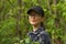 Portrait of traveler smiling young woman in black cap and glasses breathing fresh air in the green spring forest.