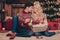 Portrait of two attractive sweet tender dreamy married spouses sitting on carpet decorating fir tree newyear custom