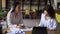 Portrait of two attractive women having a conversation in a library with shelves of books on background. Sitting at the