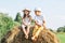 Portrait of two barefoot children boy and girl sitting on haystack in field. Smiling and laughing kids wearing hats.