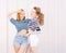 Portrait of two beautiful fashionable girlfriends in denim shorts and striped t-shirt posing nex to the glass wall. Girl holding