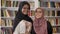 Portrait of two charming young muslim womens standing in library and smiling in camera, african muslim women in hijab