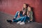 Portrait of two cute little sisters dressed in trendy clothes leaning on a wall while sitting on a skateboard at a