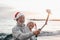 Portrait of two cute old persons having fun and enjoying together at the beach on christmas days at the beach wearing Christmas