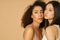 Portrait of two gorgeous mixed race young women with perfect skin looking away while posing isolated over beige