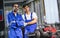 Portrait two handsome male mechanics wearing uniform, using machine for fix, repair car or automobile components, teamwork helping