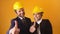 Portrait of two happy architects wearing yellow hard hats showing thumbs-up