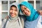 Portrait of two happy hijab women, smiling at the camera while embracing in front of their house