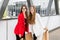 Portrait of a two happy women dress in stylish suits are standing together in front of the shopping mall with a lots of paper bags