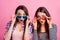 Portrait of two impressed pretty girls hands touch glasses open mouth isolated on pink color background