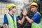 Portrait of two industrial engineer workers man wearing helmet doing high-five hand touch, standing at manufacturing plant factory