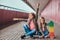 Portrait of two little sisters dressed in trendy clothes sitting together on a skateboard at bridge footway.
