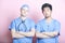 Portrait of two male surgeons standing with arms crossed over pink background