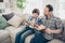 Portrait of two nice attractive focused cheerful smart clever guys dad and pre-teen son sitting on couch reading