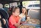 Portrait of two positive smiling sisters eating just cooked italian pizza sitting in child car seats on car back seat. Happy