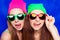 Portrait of two pretty sisters in hats and glasses showing tongue