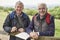 Portrait Of Two Retired Male Friends On Walking Holiday Resting On Gate With Map