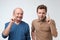 Portrait of two serious mature men father and son with warning finger against light gray background.