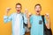 Portrait of two shocked teenagers, guys show victory gesture, on yellow background