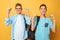 Portrait of two shocked teenagers, guys show victory gesture, on yellow background