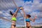 Portrait of two slim sporty girls playing beach volleyball against a bright blue sky