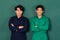 Portrait of two smart and handsome young Asian men dressed in blue and green mechanic coveralls stand confidently with crossed