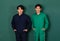 Portrait of two smart and handsome young Asian men dressed in blue and green mechanic coveralls stand confidently with crossed