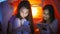 Portrait of two teenage girls typing message in social media on mobile phones in bedroom at night