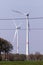 A portrait of two wind turbines standing in a field with red markings. In front of them there are some electricity power lines.