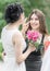 Portrait of two young beautiful women friends. Pretty bride with roses bouquet helping her smiling bridesmaid. Wedding at Sunny su
