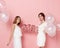 Portrait of two young cheerful friends, dressed in a white, holdings a balloons, over pink background.