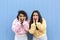 Portrait of two young women on a blue background They have their hands on their faces and are screaming in fear. Concept of terror