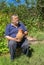 Portrait of Ukrainian senior peasant sitting on a log and taking an ancient clay jug