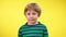 Portrait of uncertain cute Caucasian boy shrugging shoulders looking at camera. Doubtful unsure kid posing at yellow