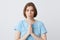 Portrait of unhappy depressed young woman in blue t shirt keeps hands folded in praying position and making sad face isolated over