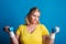 Portrait of an unhappy overweight woman with dumbbells in studio on a blue background.