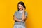 Portrait of unhappy young Asian woman while receiving incoming call on smartphone on yellow background