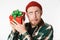 Portrait of unshaved man wearing hat and plaid shirt holding present box, while standing isolated over white background