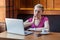 Portrait of unwell young adult woman with short blonde hair in pink t-shirt and eyeglasses sitting in cafe and touching cheek with