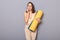 Portrait of upset brown haired sporty woman wearing beige tracksuit holding yoga mat  on gray background, talking smart