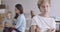 Portrait of upset Caucasian boy with grey eyes looking back at his sister and mother playing, turning back and looking