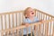 Portrait of upset crying baby standing in crib getting hysterical seeking attention of parents