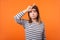 Portrait of upset disappointed young woman with brown hair in long sleeve striped shirt. indoor studio shot isolated on orange