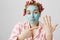 Portrait of upset funny housewife in hair-curlers pyjamas and blue face mask pointing at left arm, asking where is her