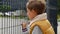 Portrait of upset little boy feeling alone looking through metal fence. Child depression, problems with bullying, victim in school