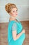 Portrait of a very beautiful, sweet, feminine and tender pregnant blonde girl with green eyes in a blue dress with rhinestones on