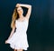 Portrait of very beautiful young blond woman in a short white dress posing on the street near a black wall. Sunny day. The wind bl